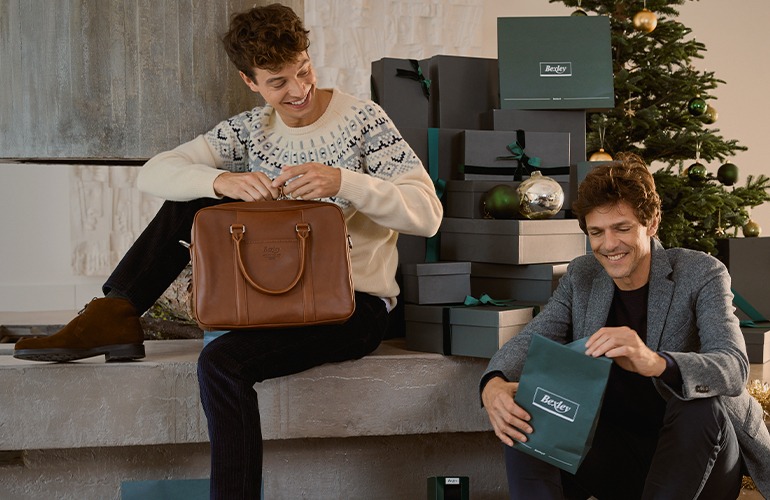 Joven desempaquetando un regalo elegante cerca de un árbol de Navidad.