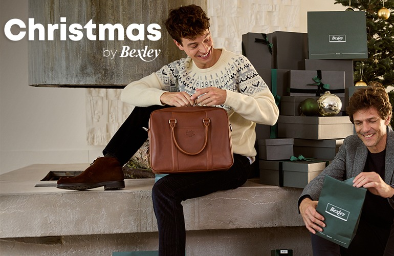 Young man unpacking an elegant gift near a Christmas tree.