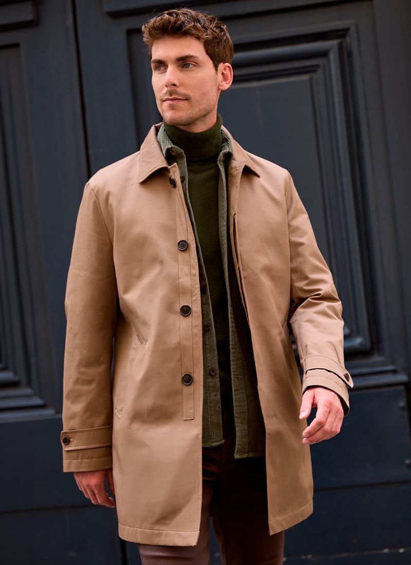 Man wearing a beige coat over a green turtleneck sweater