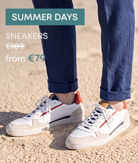 Men's white leather sneakers with navy and orange details, worn with blue linen trousers
